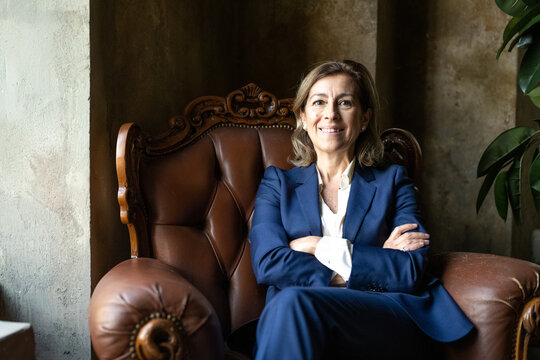 Confident Stylish European Mature Woman Sitting At Workplace, Stylish Older Senior Business Woman, Middle Aged Lady Executive Leader Manager Looking At Camera In Office, People Portrait