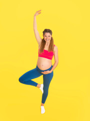 Pregnant woman performing yoga exercise in tree pose with raised hand in studio