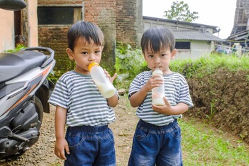 Twin asian boys are drinking milk in the yard