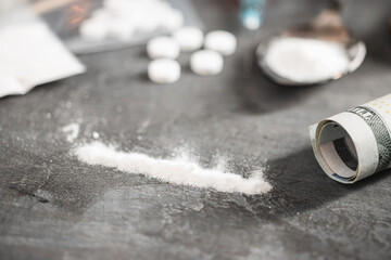 Line of white powder narcotics, white pills and rolled US dollar banknote on dark background....