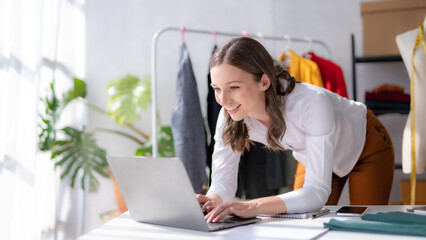 Female fashion designer sitting happily working on computer laptop.