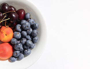 Organic ripe berries and fruits in the white bowl. Close up. Copy space