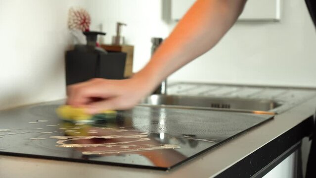 A man cleans an electric cooktop on a kitchen counter - scrubs it with a sponge - closeup