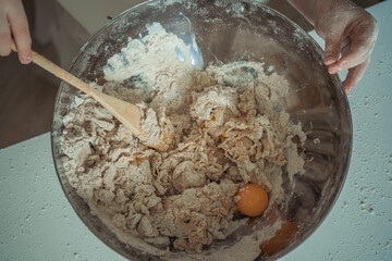A person mixing a bowl with flour and yellow egg in it by wooden spoon