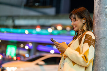 Young Asian woman listening to the music on earphones and mobile phone application during travel in the city at night. Attractive girl have fun outdoor lifestyle using portable device with internet. © CandyRetriever 