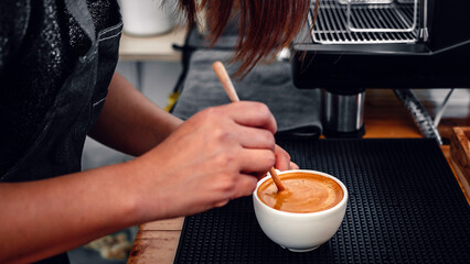 barista making coffee, the hand of a barista with a wooden spoon making or preparing coffee foam in a cup of coffee.