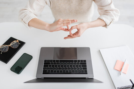 cropped view of teacher showing interpretation sign on body language near laptop and smartphone on desk.