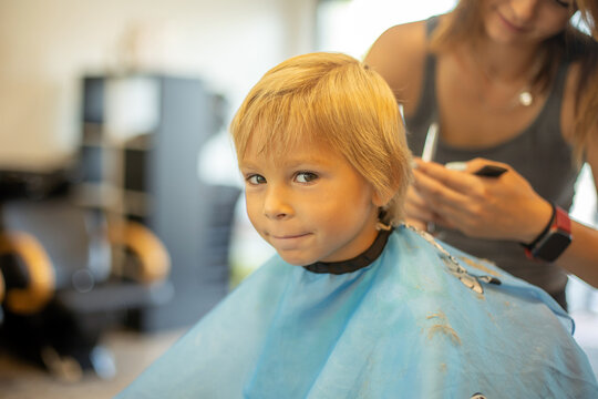 Cute toddler blond boy, having haircut in hairdresser salloon