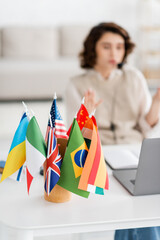 selective focus of international flags near blurred laptop and young language teacher working at home. © LIGHTFIELD STUDIOS
