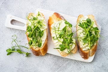 Toast with cream cheese and micro greens at cutting board. Healthy food, vegetarian dish.