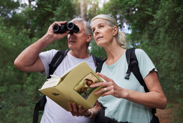 Book, bird watching and binoculars with old couple in nature for bonding, discovery and travel...