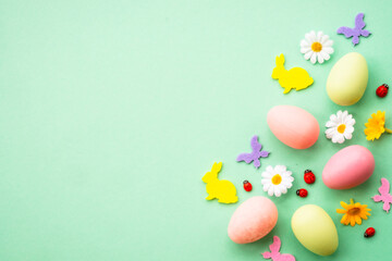 Fototapeta na wymiar Easter background. Eggs, rabbit, spring flowers and butterfly. Flat lay mock up at green background.
