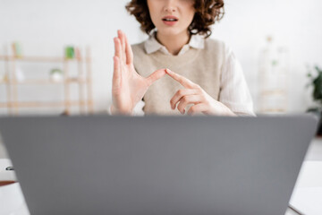cropped view of woman teaching sign language alphabet near blurred laptop at home.
