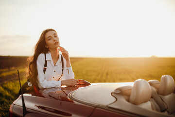 young beautiful woman in a white shirt sitting in a red car cabriolet with a white interior. red...