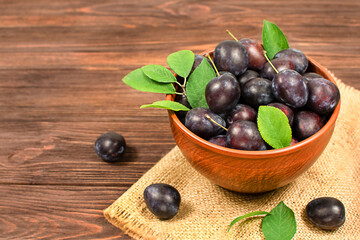 Fresh blue plums in a bowl on a wooden background. Copyspace.