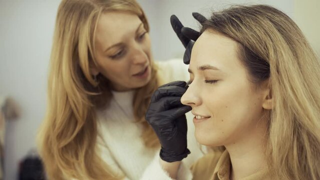 Portrait of a young woman whose eyebrows are plucked with tweezers in a beauty salon, she talks with the master during the procedure. beauty industry.
