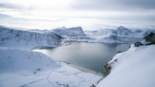 View from Mannen mouintain at Haukland beach in winter before snow storm. Blue, clean sea and snow covered mountains under grey, stormy clouds. View from Mannen peak