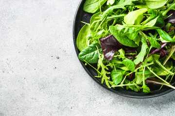 Green salad with fresh leaves assortment in black plate. Top view, close up.
