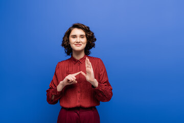 happy young teacher showing alphabet on sign language and looking at camera isolated on blue.
