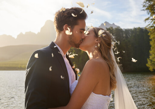 Love, wedding and confetti with a couple kissing by a lake outdoor in celebration of a marriage for romance. Water, summer or kiss with a bride and groom bonding together in tradition after ceremony