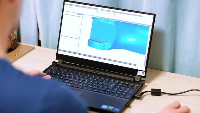 A person is working at a laptop, a 3d model of the butt is on the monitor.