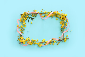 Fototapeta premium Top view image of spring yellow mimosa flowers composition over pastel blue background