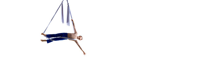 Dynamic image of young man, professional aerial gymnast, acrobat training with aerial tissue against white background. Concept of art, sportive lifestyle, action and motion. Banner. Copy space for ad