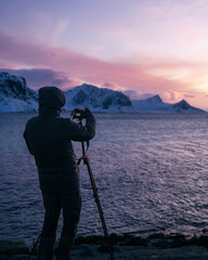 The photographer take a picture of Lofoten islands in winter. A male uses camera and tripod to...