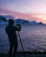 The photographer take a picture of Lofoten islands in winter. A male uses camera and tripod to capture a beautiful landscape picture at twilight in Lofoten. Majestic view of Haukland Beach. 