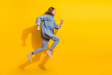 Full length photo of funky cool guy dressed jeans shirt jumping high running emtpy space isolated yellow color background