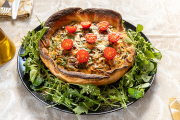 Vegetarian homemade Quiche with tomatoes, spinach, sweet pepper and cheese on black plate. with olive oil