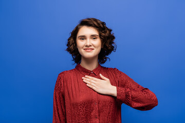 cheerful woman looking at camera and telling please on sign language isolated on blue.