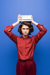 displeased student holding textbooks of foreign languages above head and looking at camera isolated...