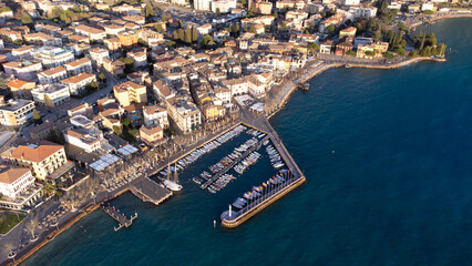 Obraz premium Aerial view with drone of the city of Garda. Town on the lake of the same name, blue sea at sunset, seagulls and boats in the distance.