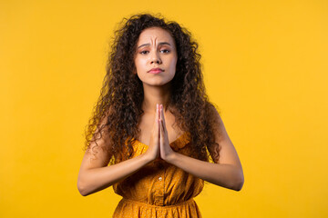 Cute woman praying, begs to apologize her, she is guilty. Yellow background. 