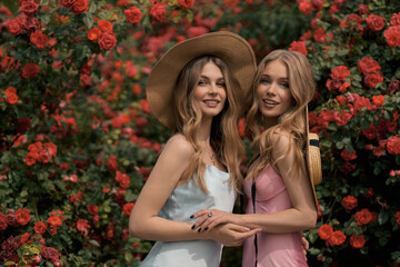 beautiful women with blond hair in elegant dress posing near bushes with blooming roses