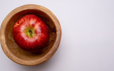 Red apple in a wooden plate close-up on a white background.
