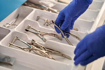 Doctor's hands wearing a disposable medical gloves holding a stainless steel nasal speculum for ENT examination over other surgery instruments