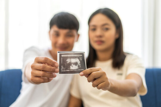 Romantic asian father and asian pregnant mother feeling happy expecting show ultrasound image,baby in belly,pregnancy,motherhood,ultrasound scan,love of family,newborn.parenthood concept