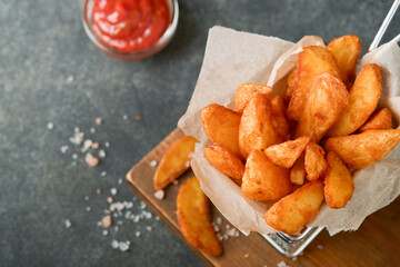 French fries in metal wire basket with salt and ketchup on old wooden dark background clous up. Fried potatoes. Fast food and unhealthy food concept.