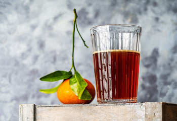 Chinotto refreshing drink in a glass on a gray wooden box with citrus fruit and gray background. Shot from below to the top in Hero concept