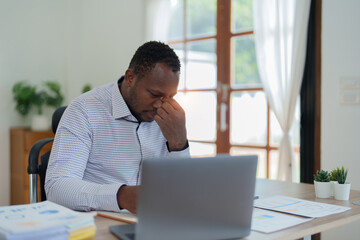 Burnout American African business man in stress works with many paperwork document, migraine attack, Freelance, work from home
