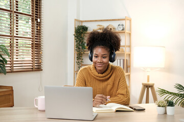 Beautiful American women student studying online takes notes on her laptop to gather information about her work smiling face and a happy study posture.