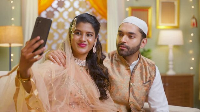 Happy Muslim couple making video call on mobile phone during Ramadan feast wishing at home - concept of technology, boding and Ramadan