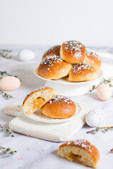 Obraz na płótnie Canvas Easter buns with caramel filling. The foreground is in blur, the middle plan is a section of a bun. On a light background with Easter attributes - eggs and willow branches