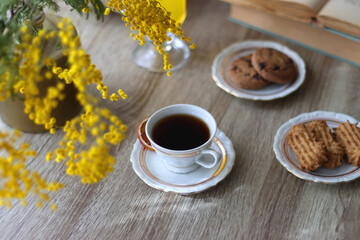 Cup of tea, plates with cookies, glass of orange juice, books, reading glasses, bowl of fruit and candles on the table. Selective focus.