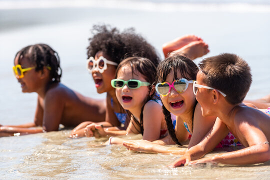Group of Diversity little child boy and girl friends lying on tropical beach and playing sea water together on summer vacation. Happy children kids enjoy and fun outdoor lifestyle on beach holiday