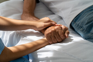 The nurse holds the hand of the elderly patient on the bed. Encouragement to recover from illness
