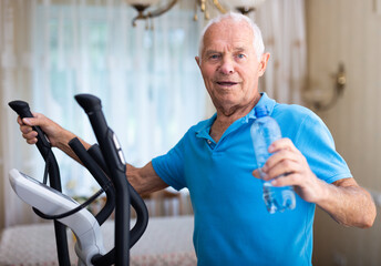 Elderly sporty man exercising on an elliptical trainer and drinking water from bottle