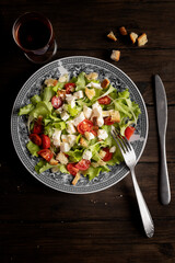 Italina salad, with lattuce salad, tomato, and mozzarella cheese, on wooden table. A glass of red wine.
